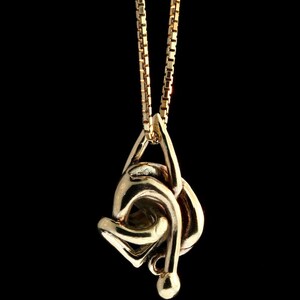May include: A gold chain necklace with a gold pendant in the shape of a knot. The pendant is intricate and detailed.
