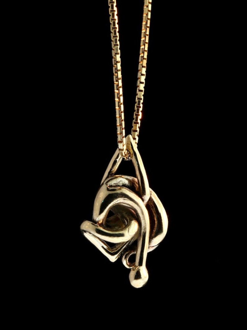May include: A gold chain necklace with a gold pendant in the shape of a knot. The pendant is intricate and detailed.