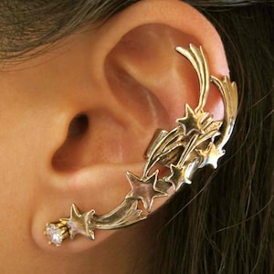 May include: Gold ear cuff with a design of shooting stars. The cuff is made of metal and has a sparkly stone at the bottom.