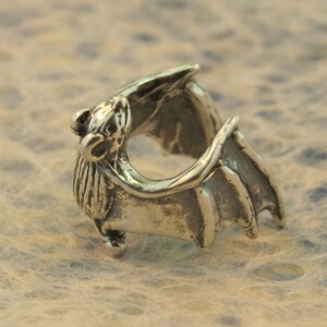 May include: A silver bat ring with detailed wings and a textured body.