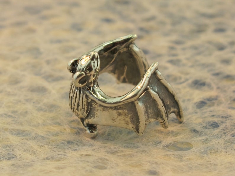 May include: A silver bat ring with detailed wings and a textured body.