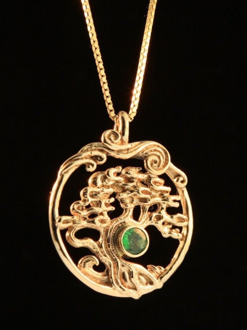 May include: A gold necklace with a pendant featuring a detailed tree of life design with a green gemstone in the center.