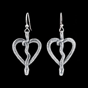 Op de afbeelding: Een paar zilveren oorbellen in de vorm van harten met een slang die om het hart is gewikkeld. De staart van de slang hangt aan de onderkant van het hart.