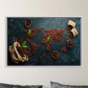May include: A framed artwork featuring a world map created from coffee beans on a dark teal surface. Coffee beans, green leaves, and small burlap sacks are arranged around the map. The artwork is displayed above a bed with gray bedding and a gold blanket.