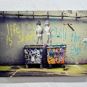 May include: A graffiti-covered wall with the words "life is short chill the f out" painted in blue and yellow. Two figures are spray-painted on the wall, and two colourful wheelie bins are in front of the wall.