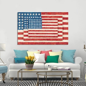 Könnte beinhalten: Ein großes Leinwandkunstwerk, das die amerikanische Flagge mit einem einzigartigen geschichteten Design darstellt. Die Flagge hat rote und weiße Streifen und ein blaues Feld mit weißen Sternen. Das Kunstwerk wird über einem weißen Sofa mit bunten Kissen gezeigt.