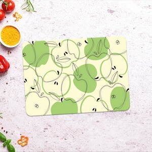 May include: A green and white kitchen placemat with a repeating pattern of apples. The apples are outlined in black and have a simple, minimalist design.