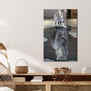 Puede incluir: Un tigre blanco reflejado en un charco de agua, mirando hacia arriba a un pequeño gatito gris y blanco de pie en el borde del charco.