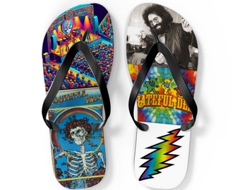 May include: Pair of black flip flops with Grateful Dead themed designs. One flip flop features a colorful illustration of a concert stage with a crowd of people, a skeleton with roses, and the text "Grateful Dead". The other flip flop features a tie-dye pattern, a dancing bear, and the text "Grateful Dead".
