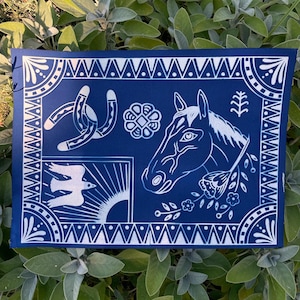 May include: A navy blue rectangular textile with a white graphic design featuring a horse head, horseshoe, bird, and floral elements. The design is framed by a decorative border.