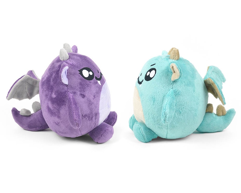Peut inclure: Deux peluches en forme de dragon, l'une violette et l'autre bleue, avec de grands yeux et des ailes.