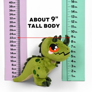 Puede incluir: Juguete de dinosaurio de peluche verde con ojos rojos y un cuerno en la cabeza. El juguete mide aproximadamente 23 cm de alto y se mide contra una regla.