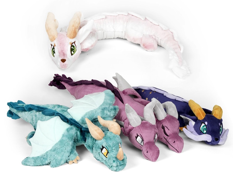 May include: Five plush dragon toys in different colors and designs. The dragons are all lying down with their wings spread out. The colors include pink, purple, teal, and blue.