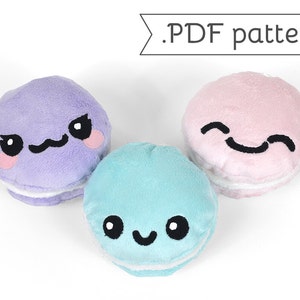 Könnte beinhalten: Drei Plüsch-Macarons mit verschiedenen Gesichtsausdrücken. Die Macarons sind lila, rosa und blau. Die Macarons haben einen weißen Zuckerguss und schwarze Augen und Münder.