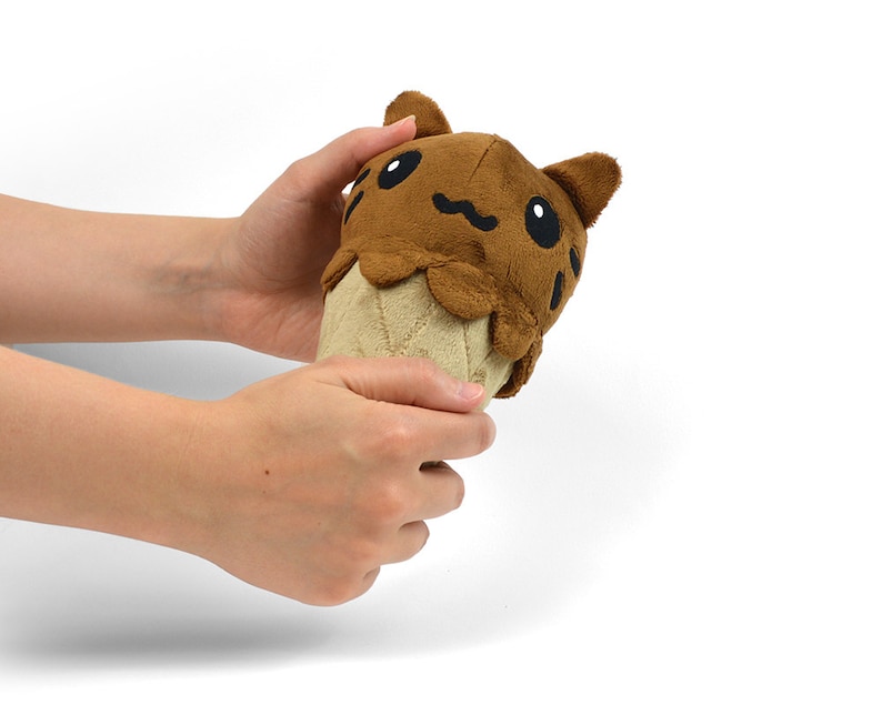 May include: A brown plush toy shaped like an ice cream cone with a cat face on top. The cat has black eyes and a brown nose.