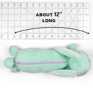 May include: A light green plush bunny pencil case with a purple zipper. The pencil case is approximately 12 inches long.