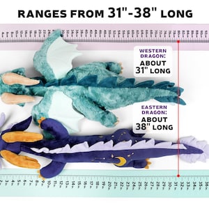 May include: Two plush dragon toys, one teal and one purple, are laid out on a white surface with a ruler measuring their length. The teal dragon is 31 inches long and the purple dragon is 38 inches long. The text "RANGES FROM 31"-38" LONG" is at the top of the image.