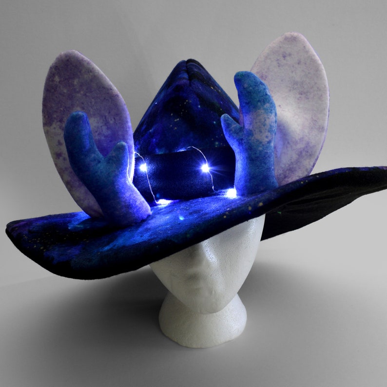 May include: A blue and purple galaxy print witch hat with light blue antlers and white LED lights. The hat is on a white mannequin head.