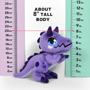 Puede incluir: Juguete de dinosaurio de peluche morado que mide 20 cm de alto. El juguete tiene una cara linda y de dibujos animados con ojos grandes y una boca peque&ntilde;a. El dinosaurio est&aacute; de pie junto a una regla.