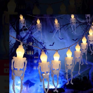May include: String of Halloween skeleton lights. Each light is a white plastic skeleton with a glowing bulb head. The background features a spooky scene with a haunted house and bats.
