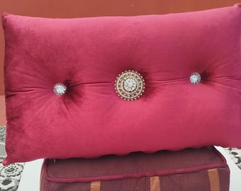 May include: A red velvet pillow with three decorative buttons. The center button is a large, round, gold-toned button with clear rhinestones. The other two buttons are smaller and clear.