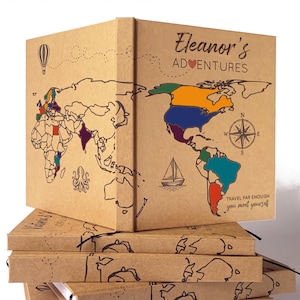 Puede incluir: Una pila de diarios de viaje con un diseño de mapa del mundo. Los diarios son marrones con un mapa de contorno negro y resaltes de países coloridos. El texto "Eleanor's Adventures" está en la portada, junto con una brújula y la cita "Travel far enough you meet yourself."