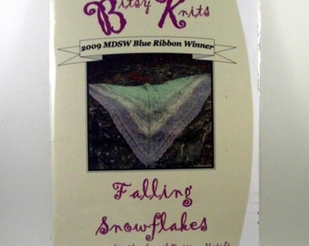 May include: A cream-colored book cover with the title "Falling Snowflakes" in purple script. The cover features a photo of a triangular shawl with a gradient of colors. The text "2009 MDSW Blue Ribbon Winner" is displayed above the photo. The brand name "Bitsy Knits" is at the top.