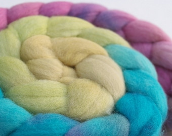 May include: A close-up of a braided yarn in shades of pink, yellow, blue, and green. The yarn is arranged in a circular pattern, creating a rainbow effect.