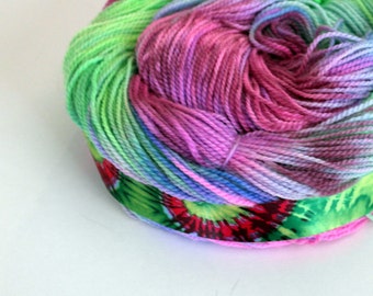 May include: A skein of hand-dyed yarn in shades of pink, green, and blue. The yarn is wrapped around a colorful fabric ribbon.