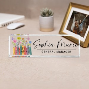 May include: A clear acrylic desk nameplate with the name "Sophia Marie" and the title "GENERAL MANAGER" in black script. The left side features colourful illustrated books with positive words and flowers.