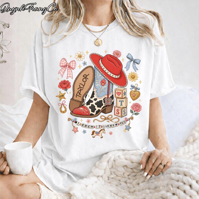 Puede incluir: Una camiseta blanca con un estampado gr&aacute;fico de una bota de vaquero con estampado de vaca, un sombrero rojo, el nombre Taylor, el n&uacute;mero 13, bloques de letras, lazos, flores, una herradura, un coraz&oacute;n y una pancarta que dice I KNEW IT I KNEW YOU.