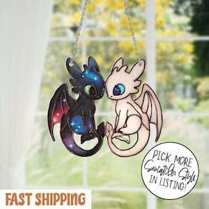 Puede incluir: Un atrapasoles con dos figuras de dragones, una negra con un diseño de estrellas y otra blanca. Están suspendidos por una cadena. El texto "Pick More Suncatcher Style in Listing!" está en un círculo.