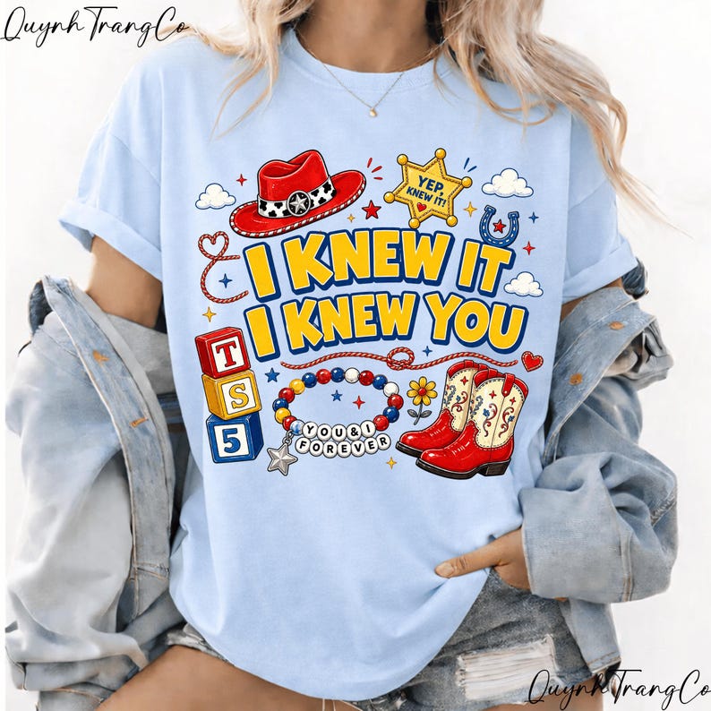 May include: A light blue t-shirt featuring a graphic print with a red cowboy hat, a yellow sheriff star badge with the text YEP, KNEW IT, red cowboy boots, a beaded bracelet with the text YOU & I FOREVER, and blocks with letters T, S, 5.