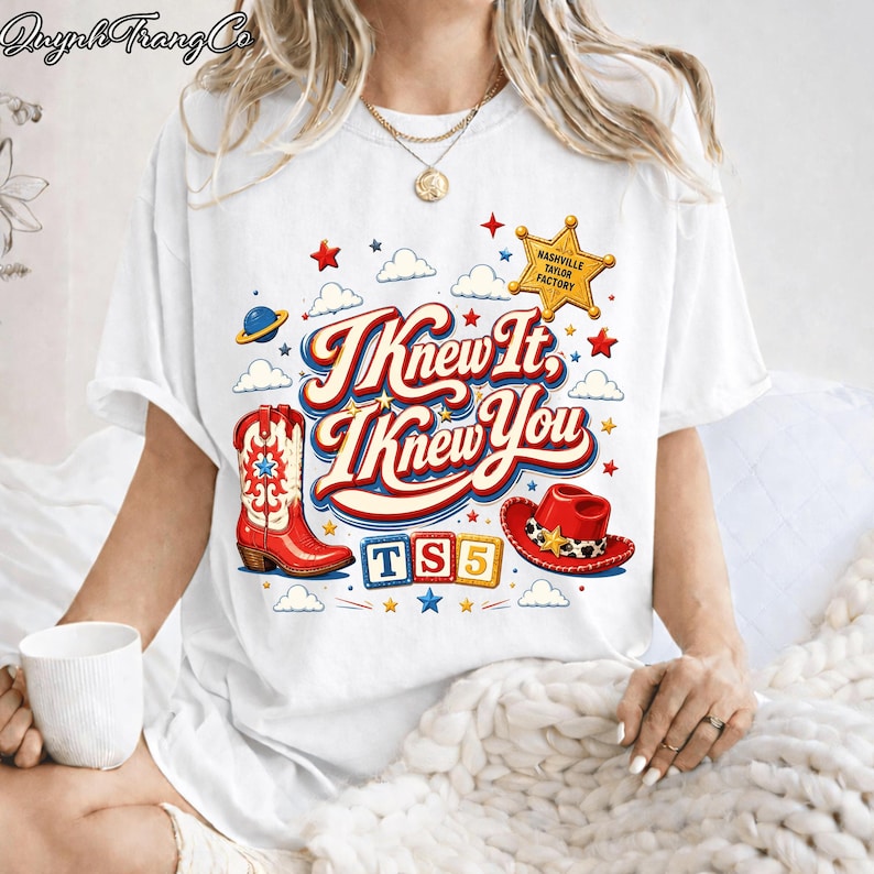 May include: A white short-sleeve t-shirt featuring a graphic print with the text "I Knew It, I Knew You" in red and blue. The design includes a red cowboy boot, a red cowboy hat, a yellow sheriff star, and colorful blocks spelling "TS5".