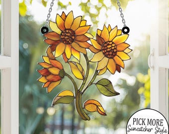 May include: Stained glass sunflower suncatcher in yellow, orange, and green. The floral design features three sunflowers on a stem with leaves, suspended by a chain. The suncatcher is displayed in front of a window.