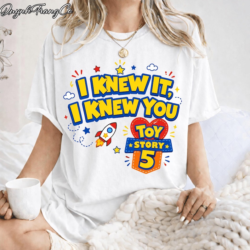 Pu&ograve; includere: Una t-shirt bianca a maniche corte con una stampa grafica colorata con il testo I KNEW IT, I KNEW YOU e TOY STORY 5. Il design include un razzo rosso e bianco, un cuore rosso, stelle gialle e nuvole blu sulla parte anteriore.