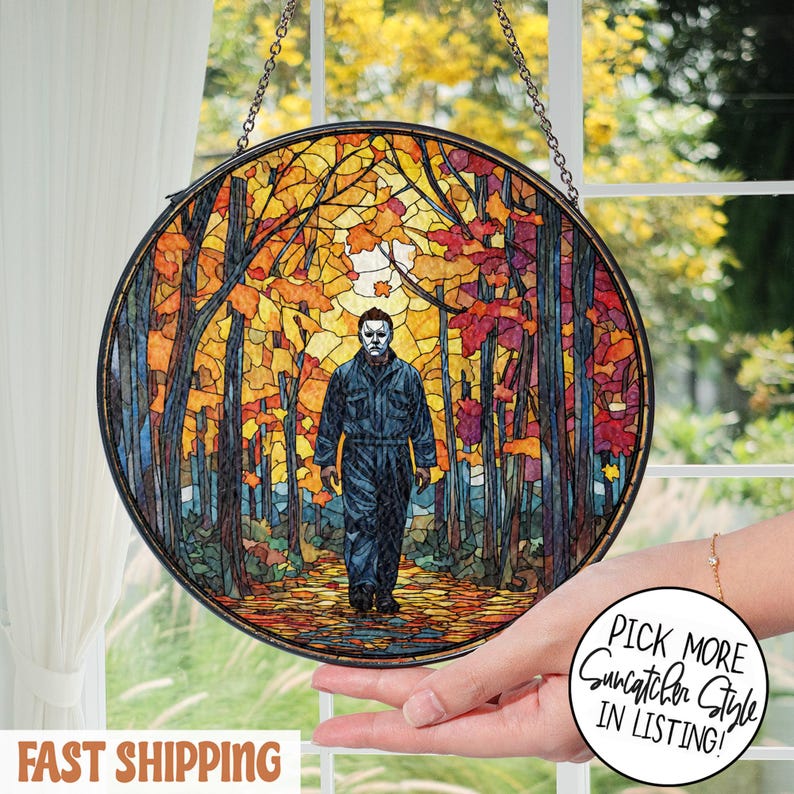 May include: Round stained glass suncatcher featuring a figure in a dark jumpsuit and mask walking through a colorful autumn forest. The artwork is framed in a black metal border and hangs from a chain. The image has the text "Pick More Suncatcher Style in Listing!"