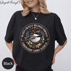 May include: Black t-shirt featuring a circular design with a bird, flowers, and the text "WHEN CRUELTY BECOMES NORMAL COMPASSION LOOKS RADICAL." The shirt has short sleeves and a crew neck. The brand name "Quynh Trang Co" is printed at the top.
