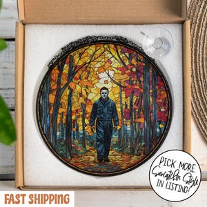 May include: Round stained glass suncatcher featuring a figure in a blue jumpsuit and mask walking through a colorful autumn forest. The artwork is framed with a black metal chain and includes a suction cup for hanging. The text "Pick More Suncatcher Style In Listing!" is visible.