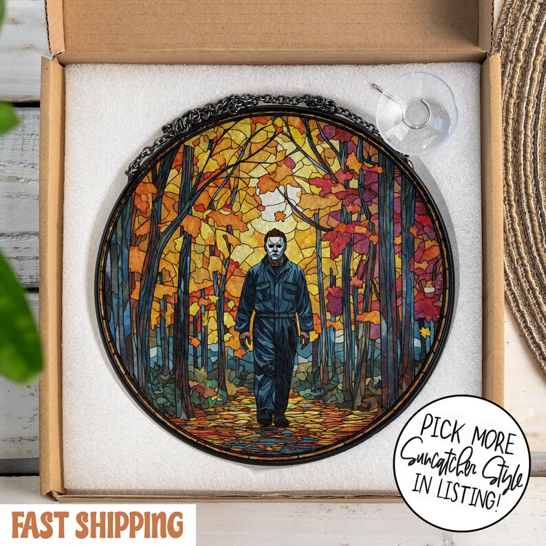 May include: Round stained glass suncatcher featuring a figure in a blue jumpsuit and mask walking through a colorful autumn forest. The artwork is framed with a black metal chain and includes a suction cup for hanging. The text "Pick More Suncatcher Style In Listing!" is visible.