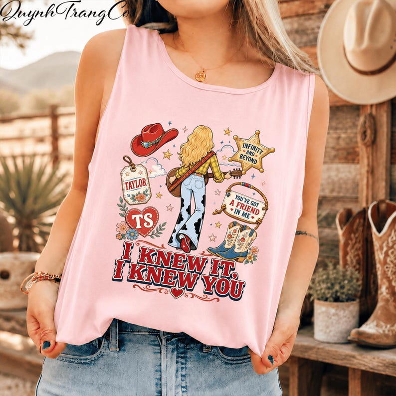 May include: A light pink sleeveless tank top featuring a graphic print of a blonde person with a guitar, a red cowboy hat, a star, a heart with the letters TS, and cowboy boots. The text reads Taylor, Infinity and Beyond, You've Got a Friend in Me, and I Knew It, I Knew You.