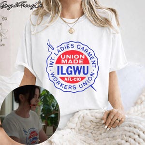 May include: White t-shirt featuring a circular graphic with the text "INT. LADIES GARMENT WORKERS UNION, UNION MADE, ILGWU, AFL-CIO." The design is in red and blue. The shirt is a casual wear item.