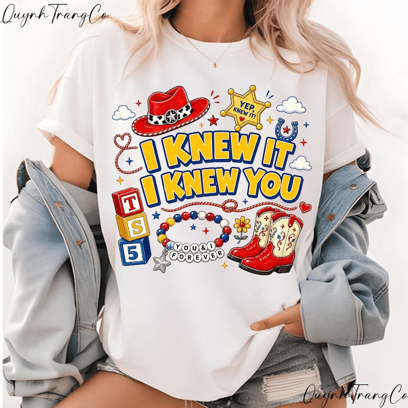 May include: A white t-shirt featuring a graphic print with the text I KNEW IT I KNEW YOU. The design includes a red cowboy hat, a yellow sheriff star, a horseshoe, red cowboy boots, alphabet blocks labeled T, S, 5, and a beaded bracelet with charms.