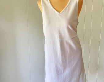 May include: White sleeveless dress with a V-neckline. The dress has a simple design with a horizontal seam at the waist. The dress is displayed on a mannequin.