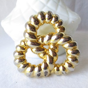 May include: A gold-toned metal brooch with a pretzel-like design. The brooch features a textured, rope-like pattern and a shiny finish. The jewelry is set against a white background, highlighting its intricate details.