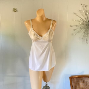 May include: A white slip dress with a beige lace trim top. The dress has thin straps and a straight neckline.