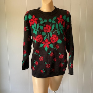 May include: A black long-sleeve knit sweater featuring a repeating pattern of red roses and green leaves. The garment has a crew neckline and ribbed cuffs and hem. The floral design is distributed across the front and sleeves of the sweater.