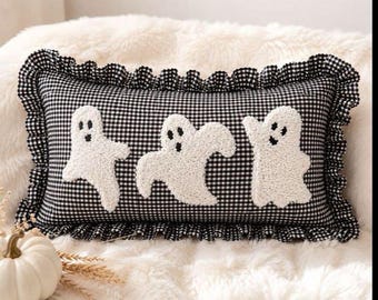 May include: A rectangular throw pillow featuring a black and white gingham pattern with a ruffled edge. The front of the pillow is decorated with three white, textured, punch-needle style ghost figures, each with black embroidered eyes and mouths.