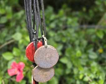 May include: A collection of circular pendants hanging from black cords. The pendants feature a mix of textured brown surfaces and glossy red finishes, each attached to the cord with a small silver-toned metal bail connector.