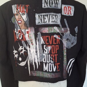K&ouml;nnte beinhalten: Schwarze, kurze Jacke mit Graffiti-Design. Sie zeigt die Worte "NOW OR NEVER", "NEVER STOP JUST MOVE" und eine Grafik eines Frauengesichts. Die Jacke hat einen klassischen Kragen und wird auf einer Schaufenquin pr&auml;sentiert.